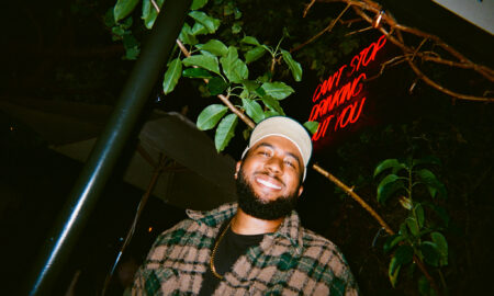 Smiling man with a beard wearing a white cap and plaid jacket outdoors at night.