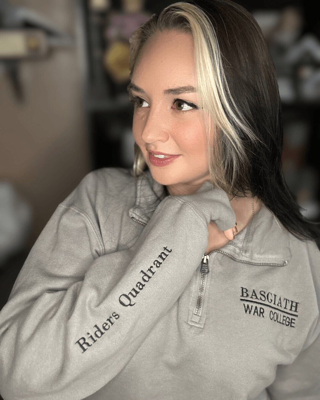 Young woman with blonde and dark hair, wearing a gray sweatshirt, looking to the side indoors.