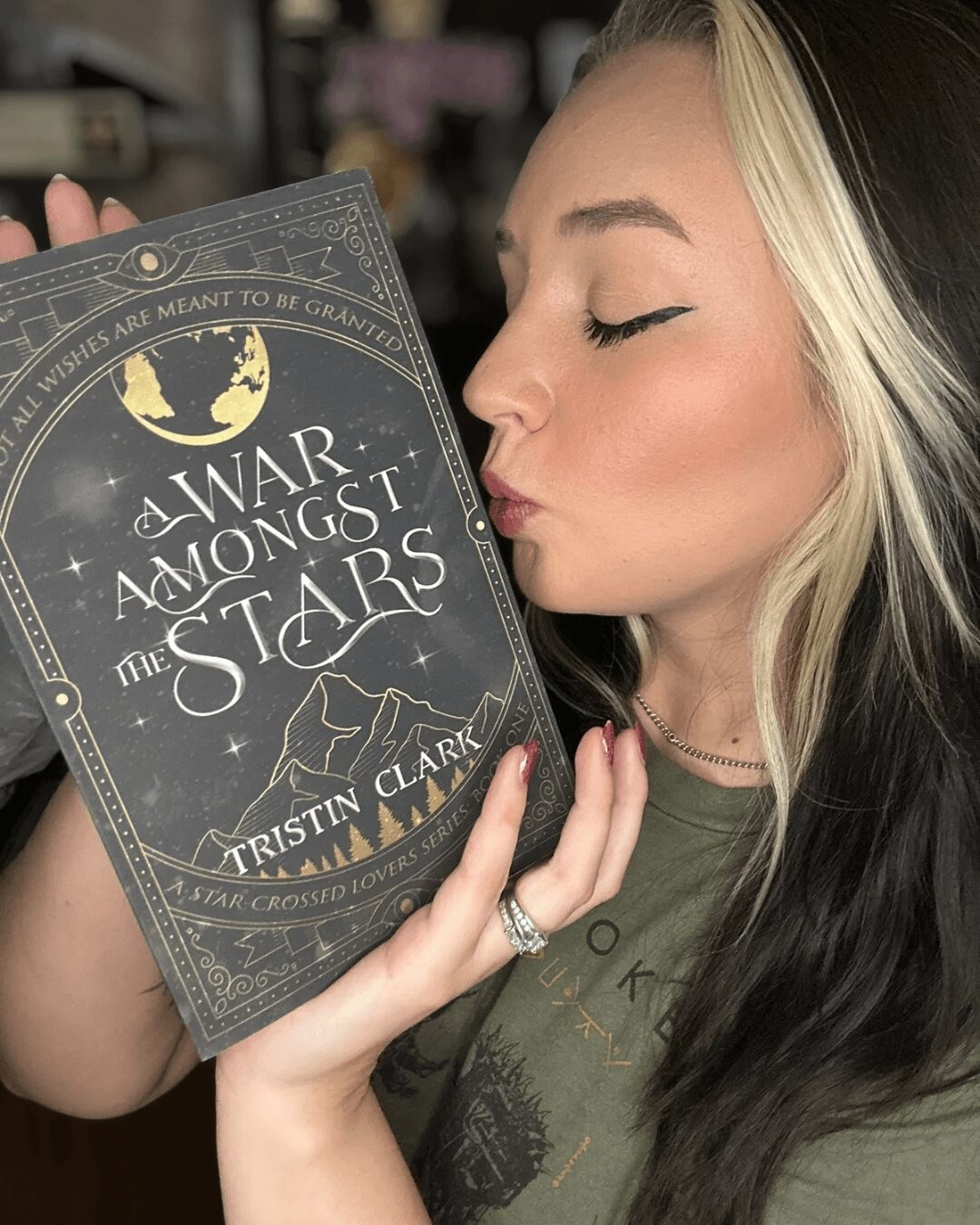 Young woman with blonde and dark hair holds a book titled 'Anar Among the Stars' close to her face, eyes closed.