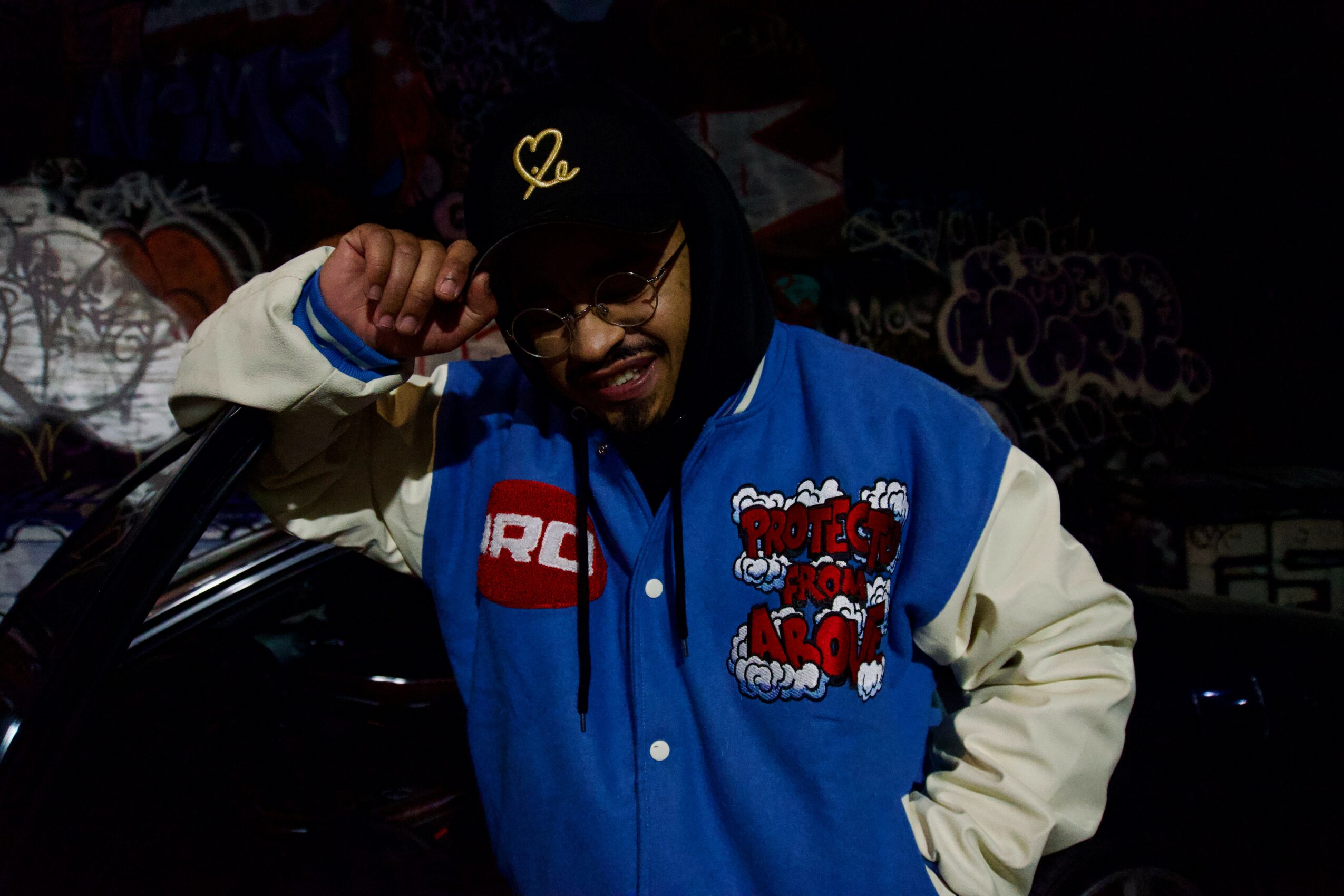 Person wearing a blue and white jacket, black cap, and glasses, smiling and adjusting the cap.