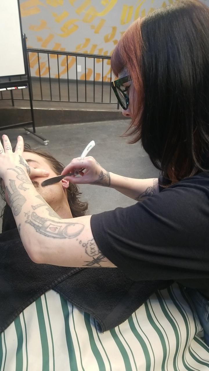 Person with black and pink hair getting a tattoo on their arm by a tattoo artist with tattoos on their arm.
