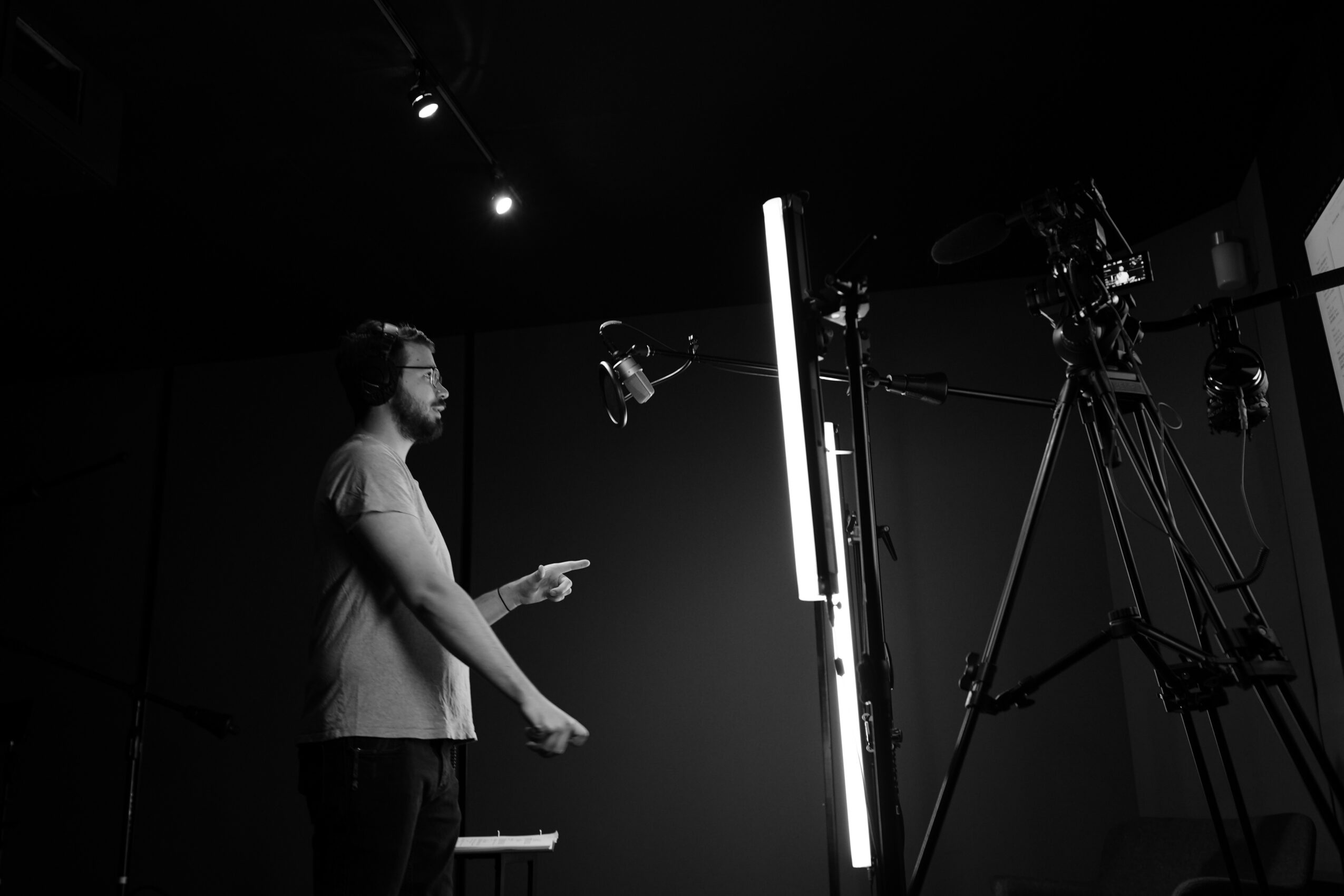 Man in a studio with professional camera equipment and lighting, pointing at a vertical screen or panel.