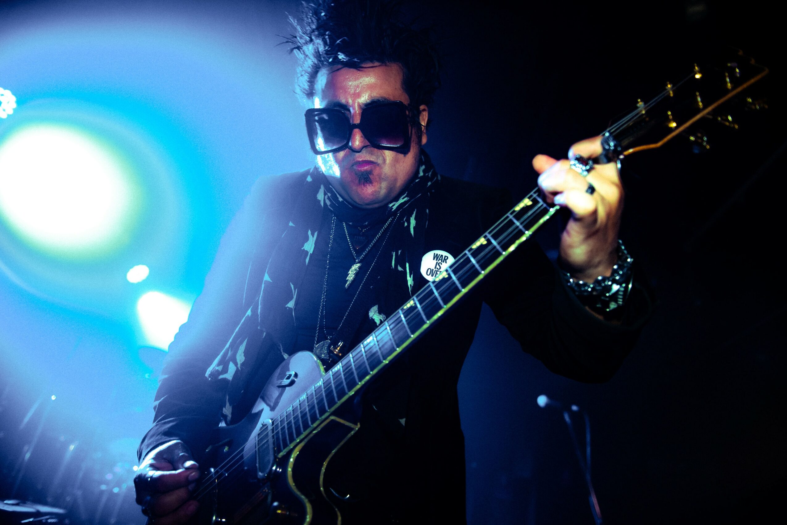 Person playing electric guitar on stage with bright blue and white lights in background.