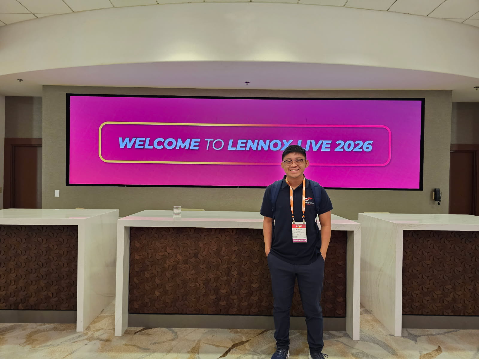 Person standing in front of a large digital screen with pink background and white text, in a spacious lobby area.