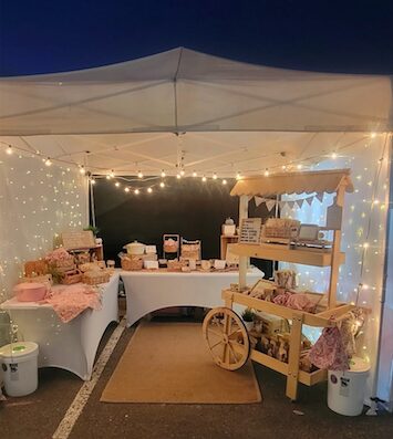 Outdoor event setup with tables, string lights, and a wooden cart under a canopy at night.