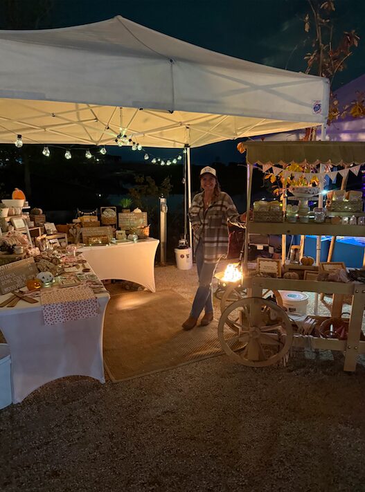 Night market stall with tables, a person, and hanging lights under a canopy.
