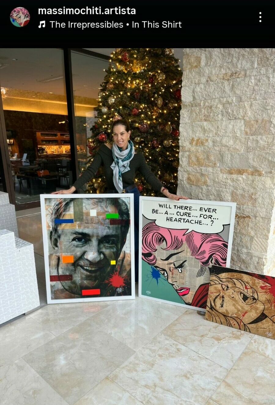 Person standing near a decorated Christmas tree with two artworks on the floor, one of a face and one of a comic character.