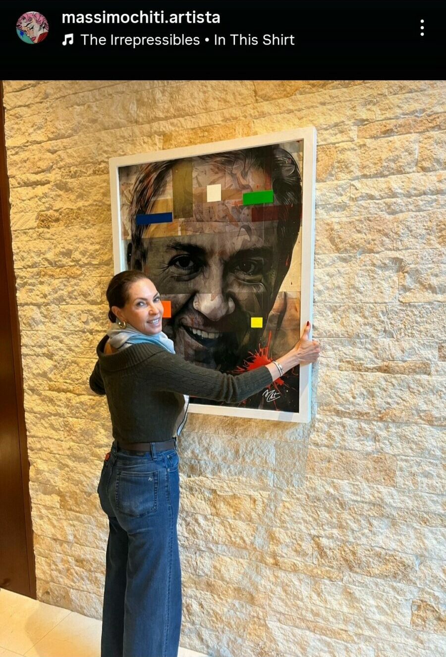 Person standing next to a framed artwork on a textured wall, touching the frame with one hand.