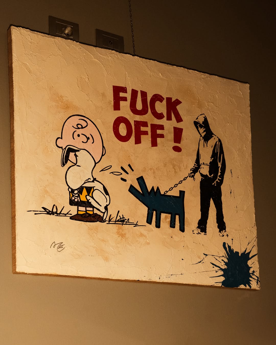 Street art with cartoon dog and person holding leash, text says 'FUCK OFF!', dark background, paint splatter in corner.