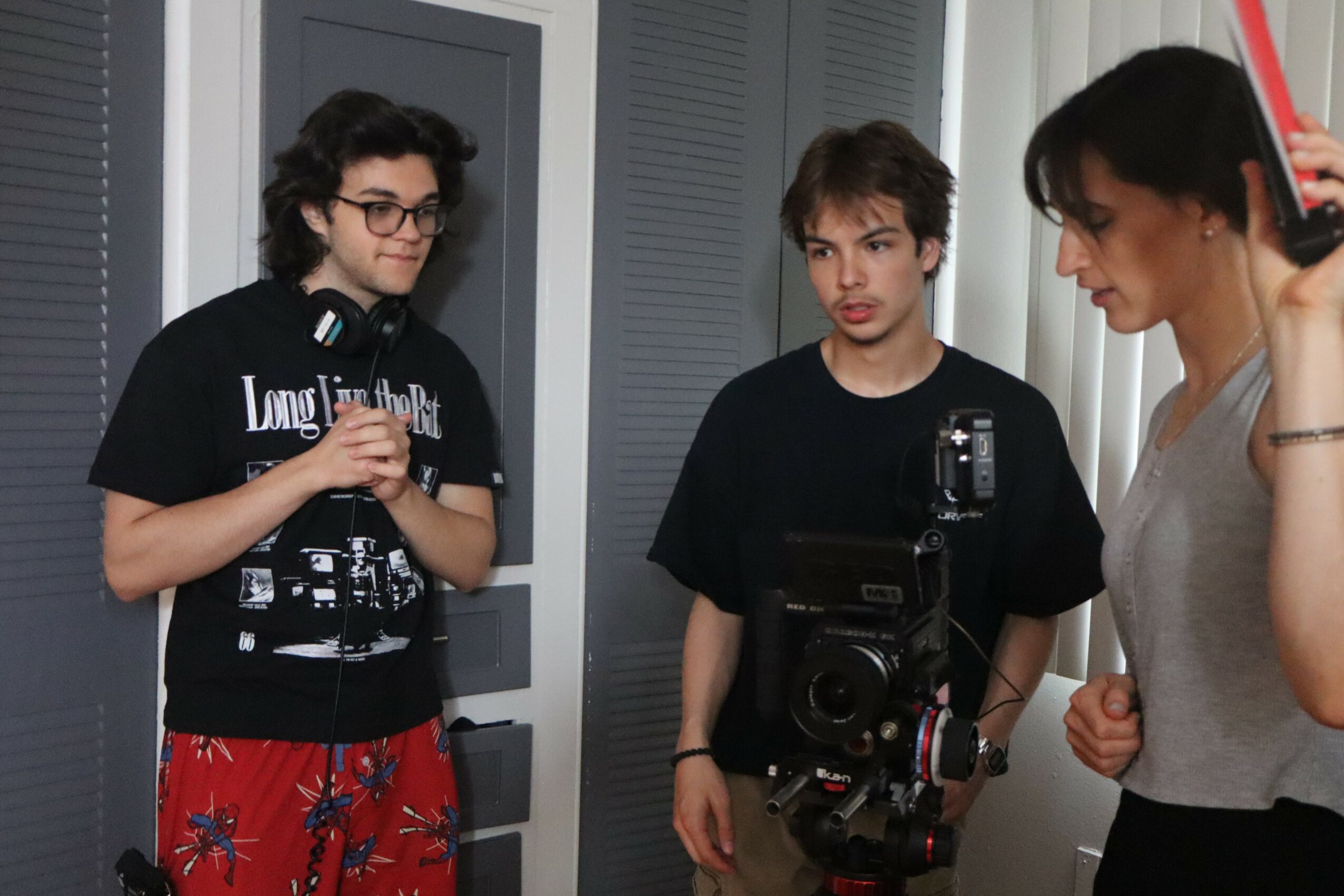 Three people standing indoors, one with a camera, engaged in conversation or activity.