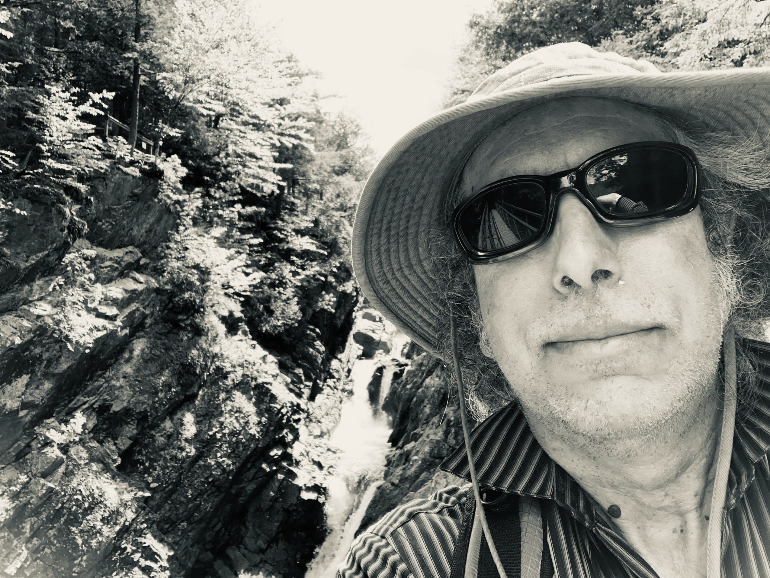 Person wearing a wide-brimmed hat and sunglasses outdoors near rocks and water.