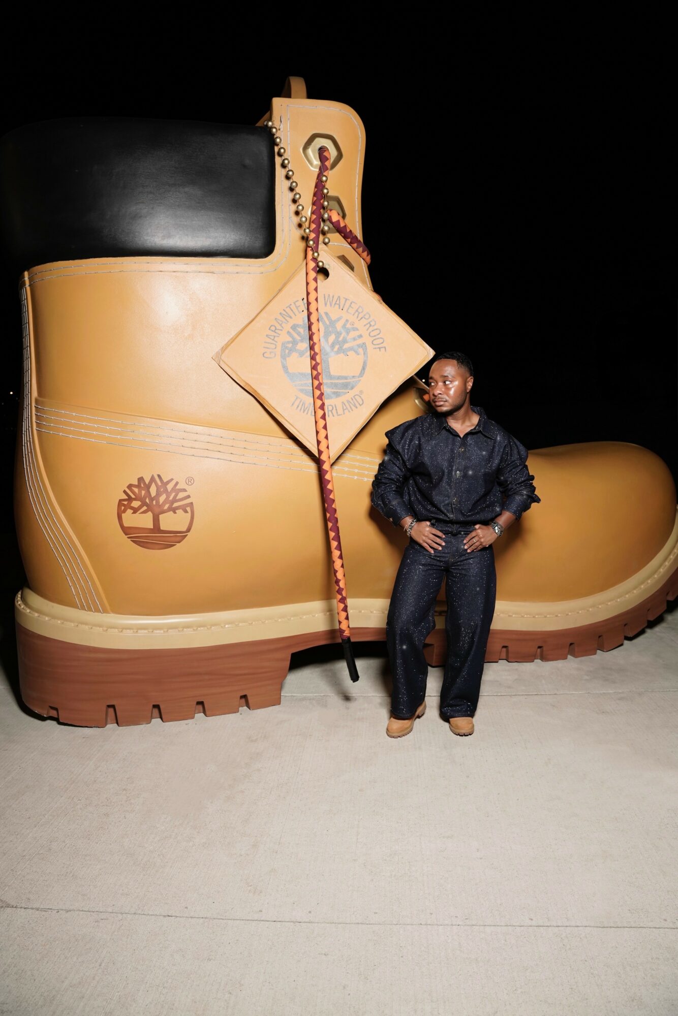 Person standing in front of a large yellow and black boot sculpture at night.
