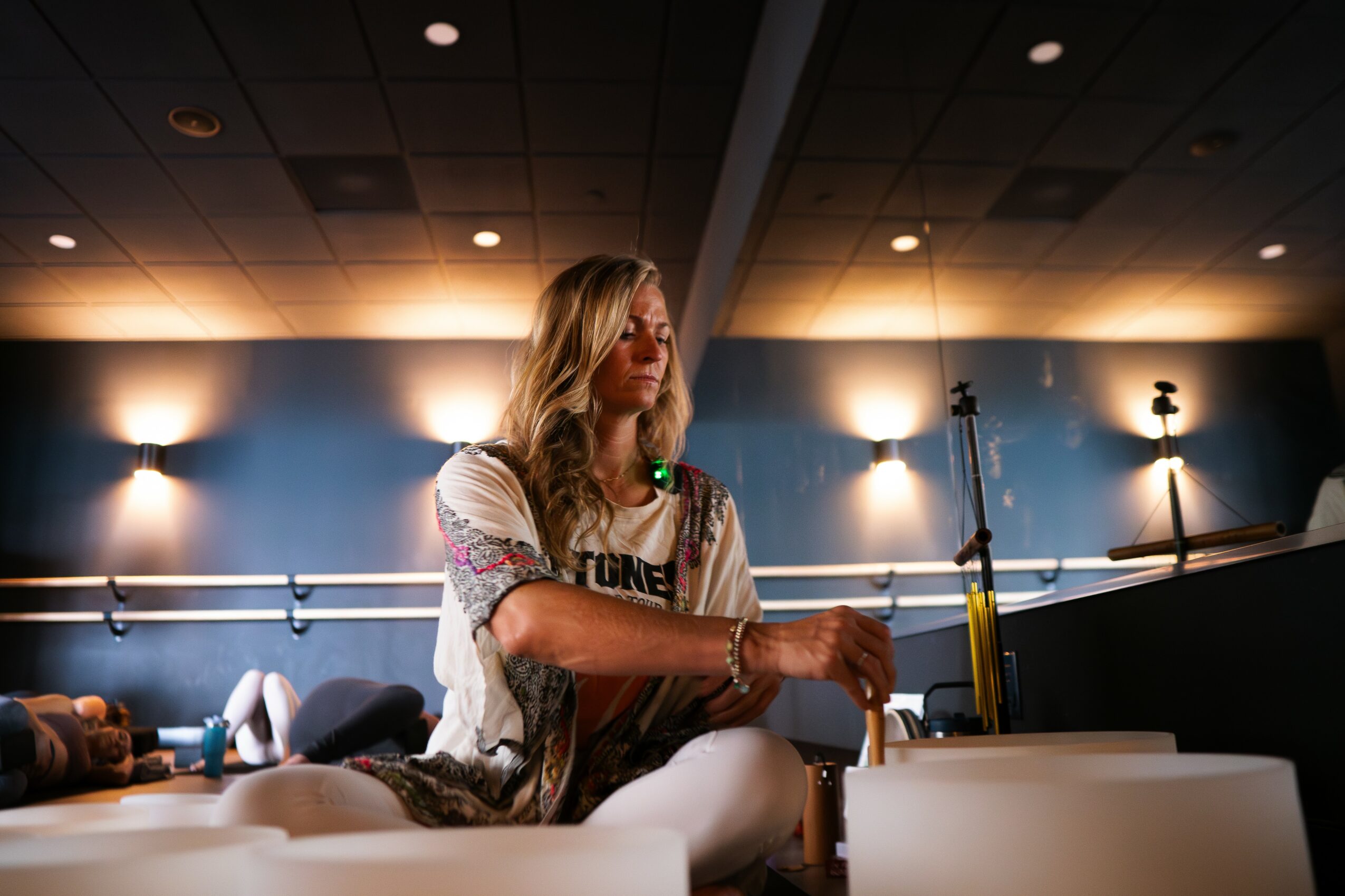 Woman with long hair sitting at a table in a room with blue walls and ceiling lights.