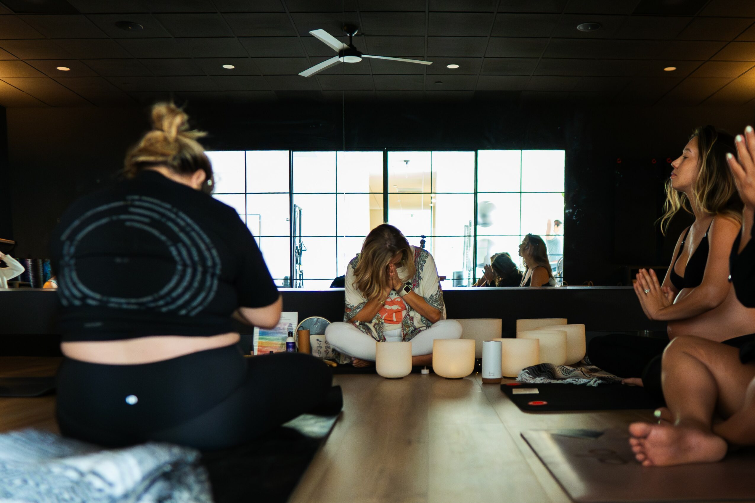 Group of women sitting around a table with candles in a room with large windows and a ceiling fan.