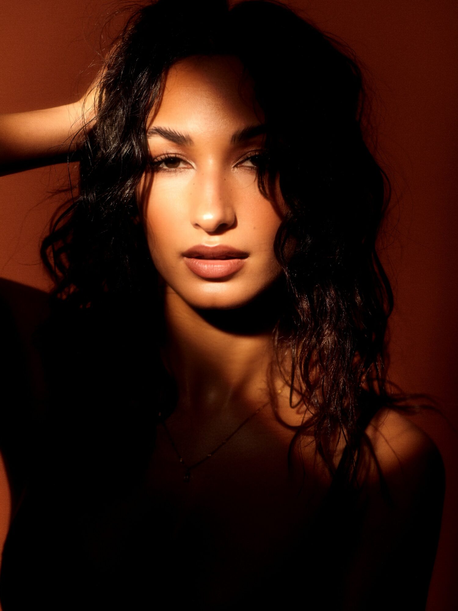 Portrait of a woman with dark, wavy hair and light makeup, looking directly at the camera with a neutral expression.