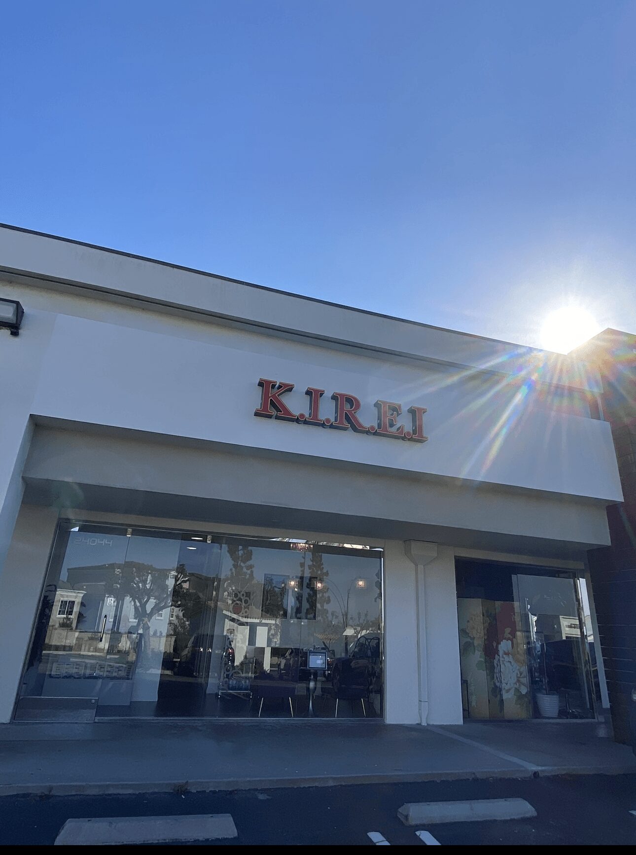 Store with a sign reading 'KIREI' and large glass windows, under a clear blue sky with sunlight.