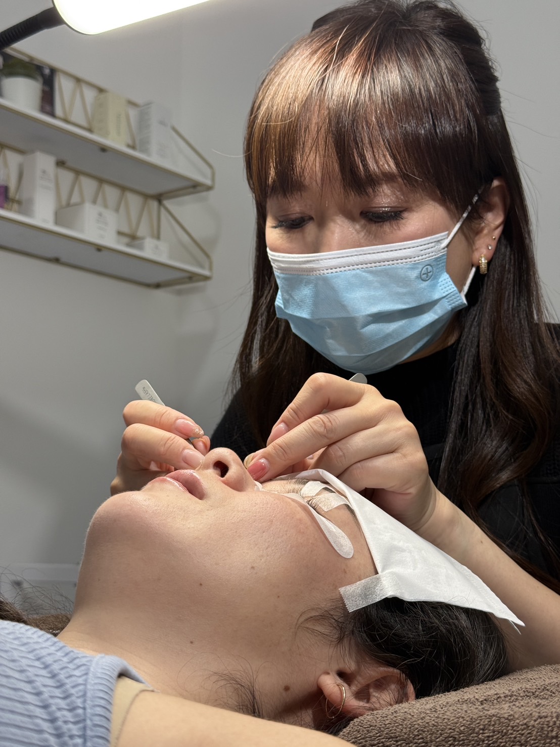Medical professional wearing a mask administers a procedure on a patient's face in a clinical setting.