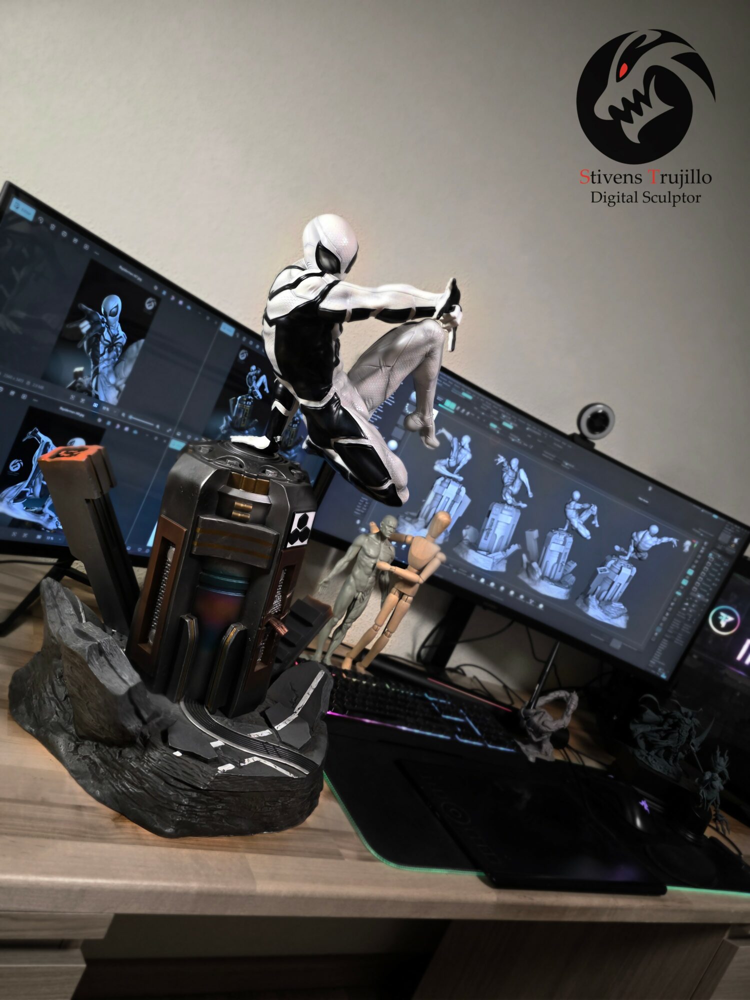 Desk with computer monitors displaying 3D character models, a sculpture of a person, and various tools and objects.
