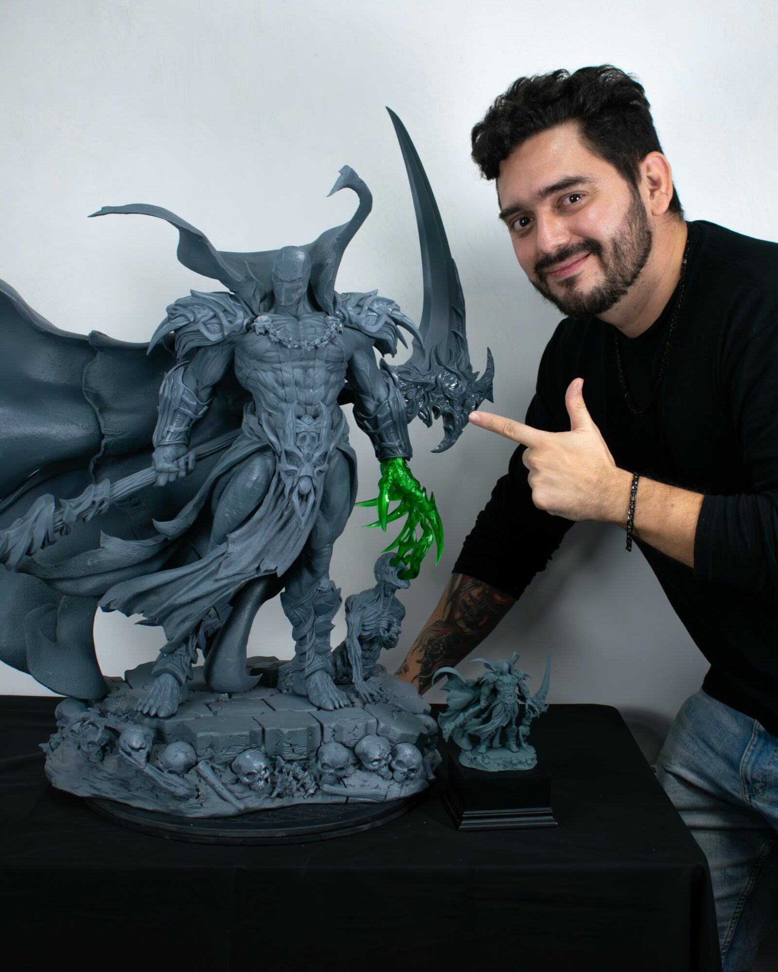 Man with dark hair and beard pointing at a large fantasy creature sculpture on a table.
