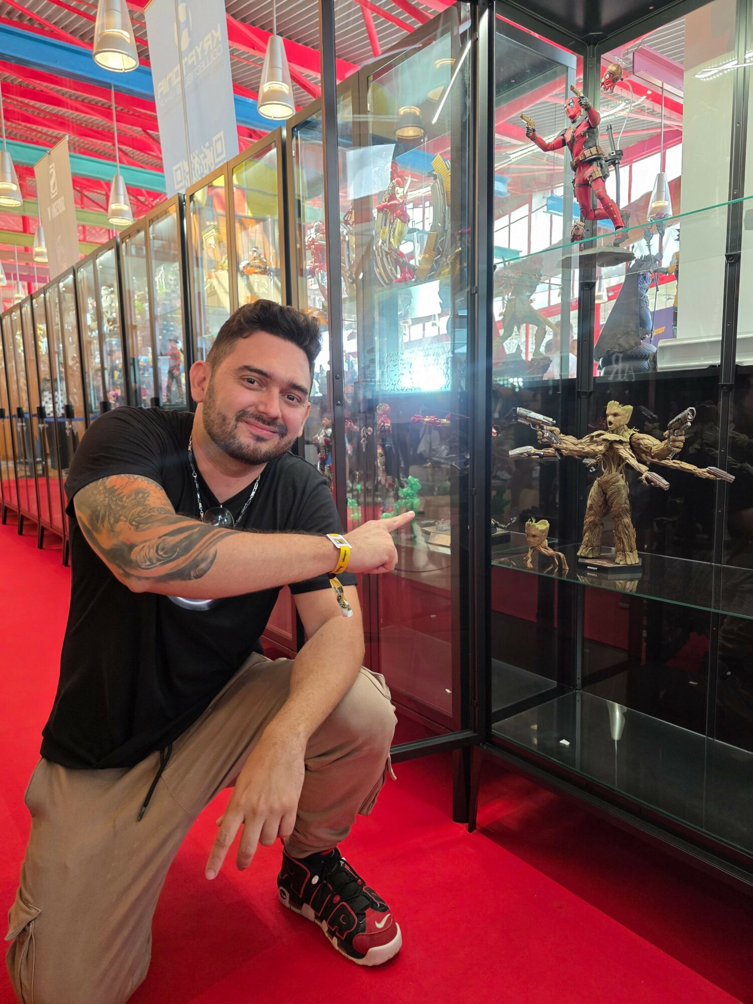 Man crouching and pointing at action figures in glass display case at an indoor amusement park.