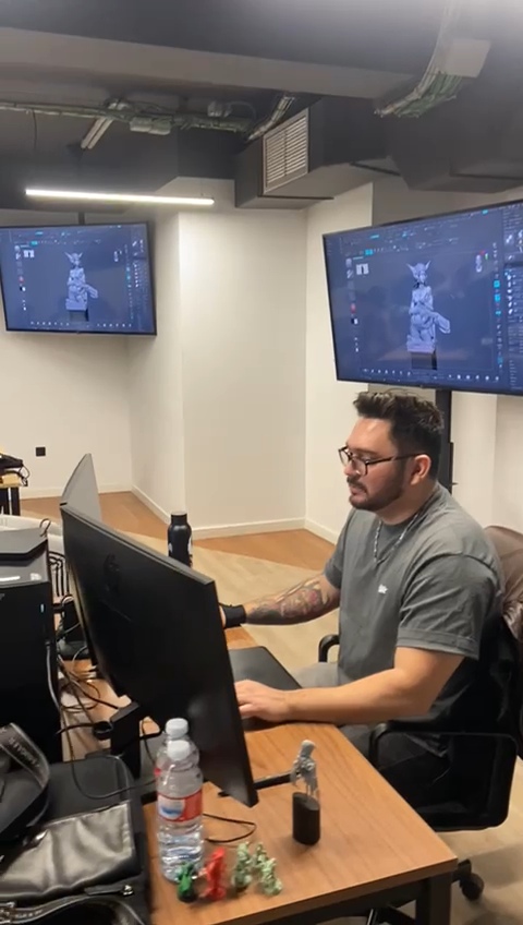Man with glasses working at a desk with multiple monitors in a room with two wall-mounted screens.