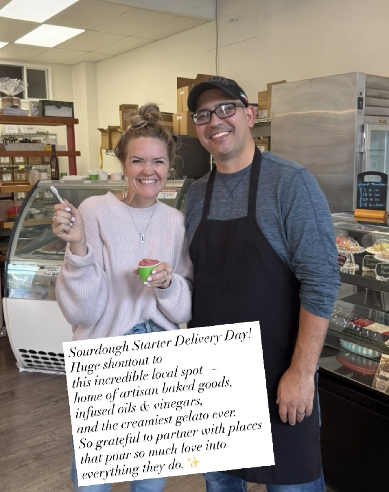 Two people smiling, one holding a small bowl, in a store with shelves and a display case behind them.