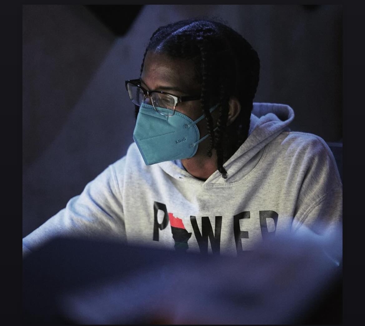 Person wearing glasses and a face mask, looking at a screen, in a hoodie with the word 'POWER' on it.