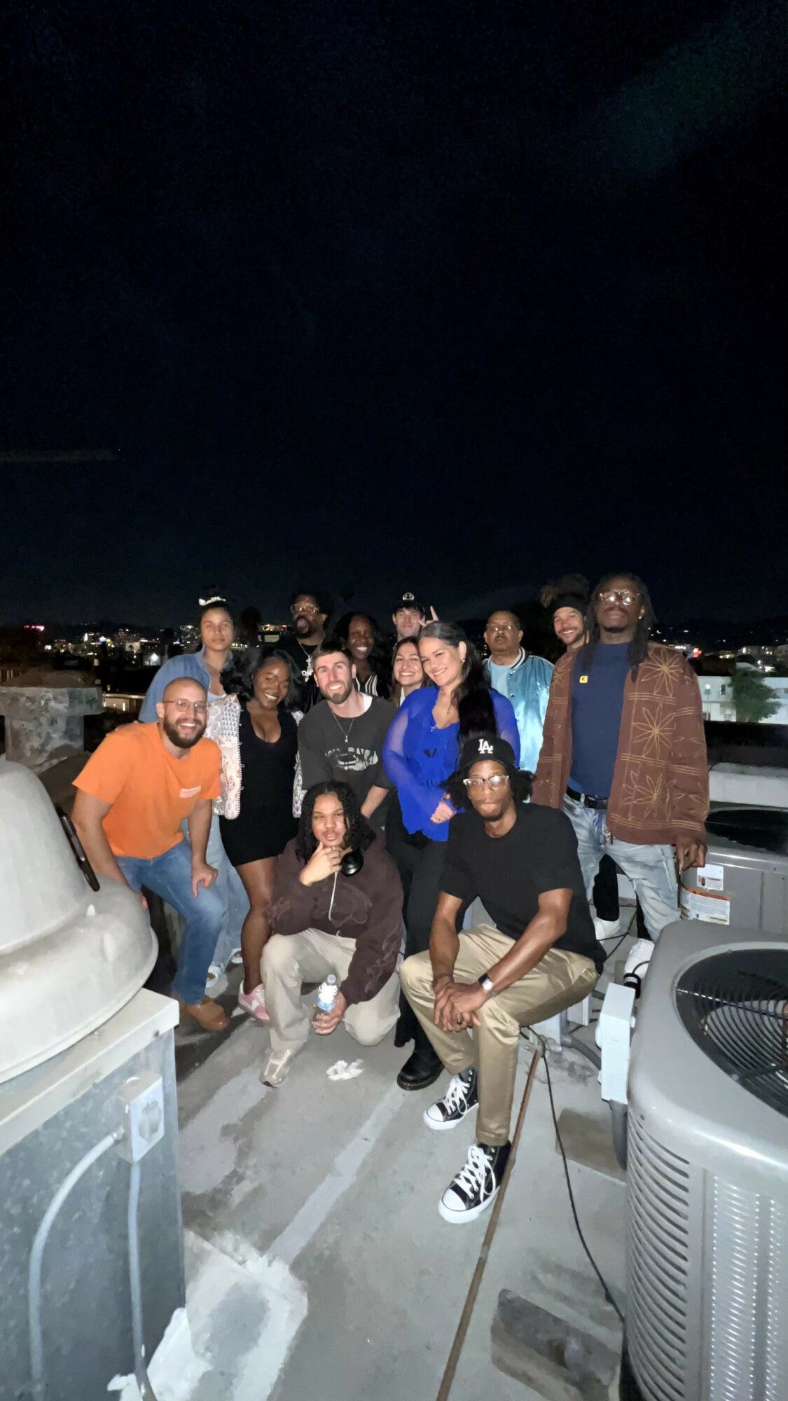 Group of people posing on a rooftop at night with city lights in the background.