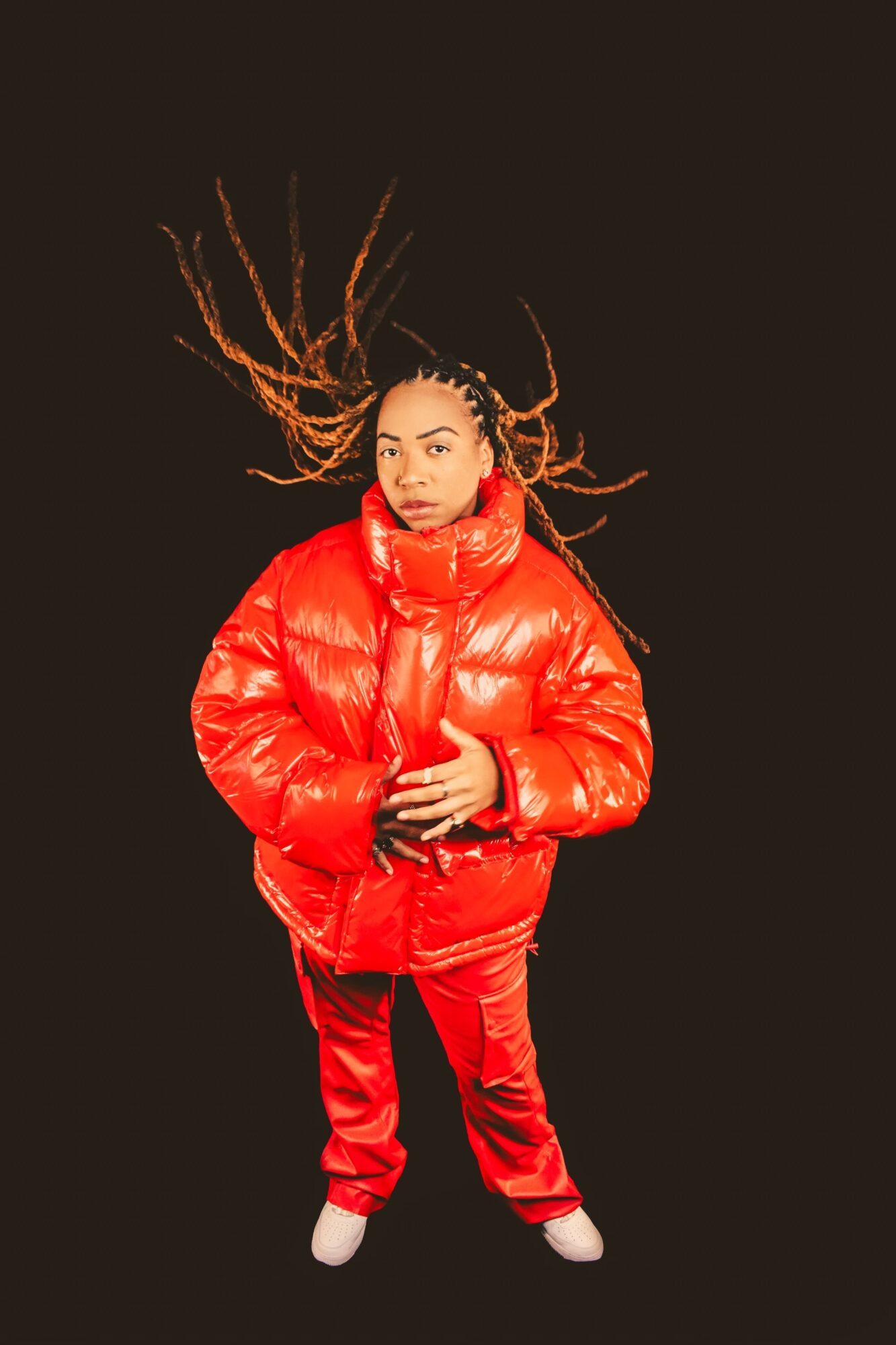 Person with long hair in motion, wearing a red puffer jacket and pants, standing against a black background.