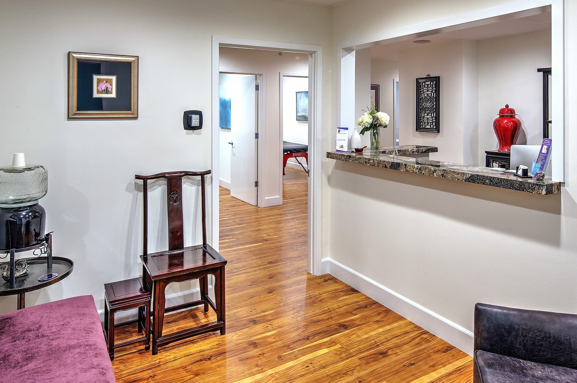 Living room with wooden floor, a wooden chair, a purple sofa, and a kitchen counter with a vase and decorative items.