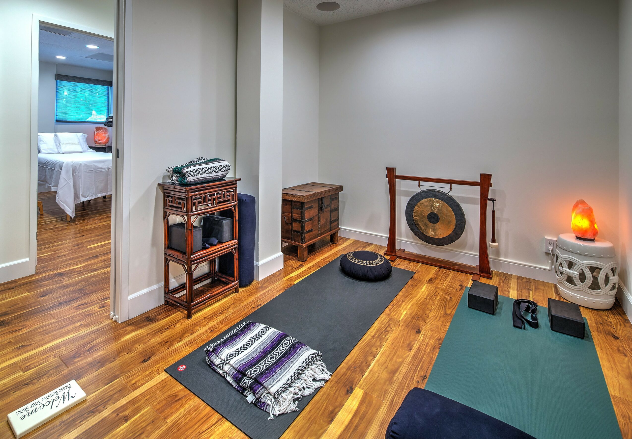 Yoga mats, gong, and meditation accessories in a room with wooden floor and white walls.