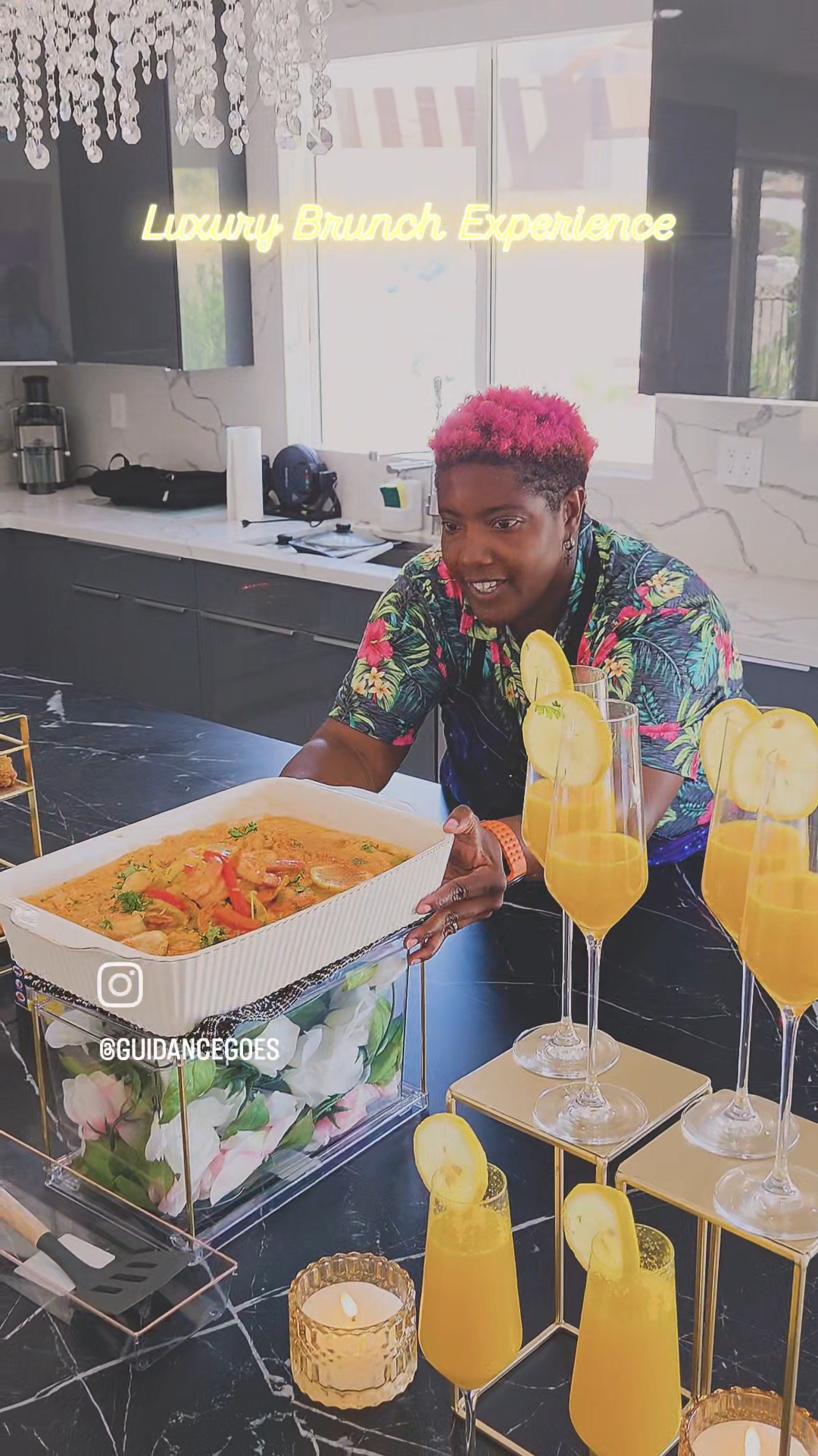 Person with pink hair serving food at a buffet table with yellow drinks and decorations, in a bright room.