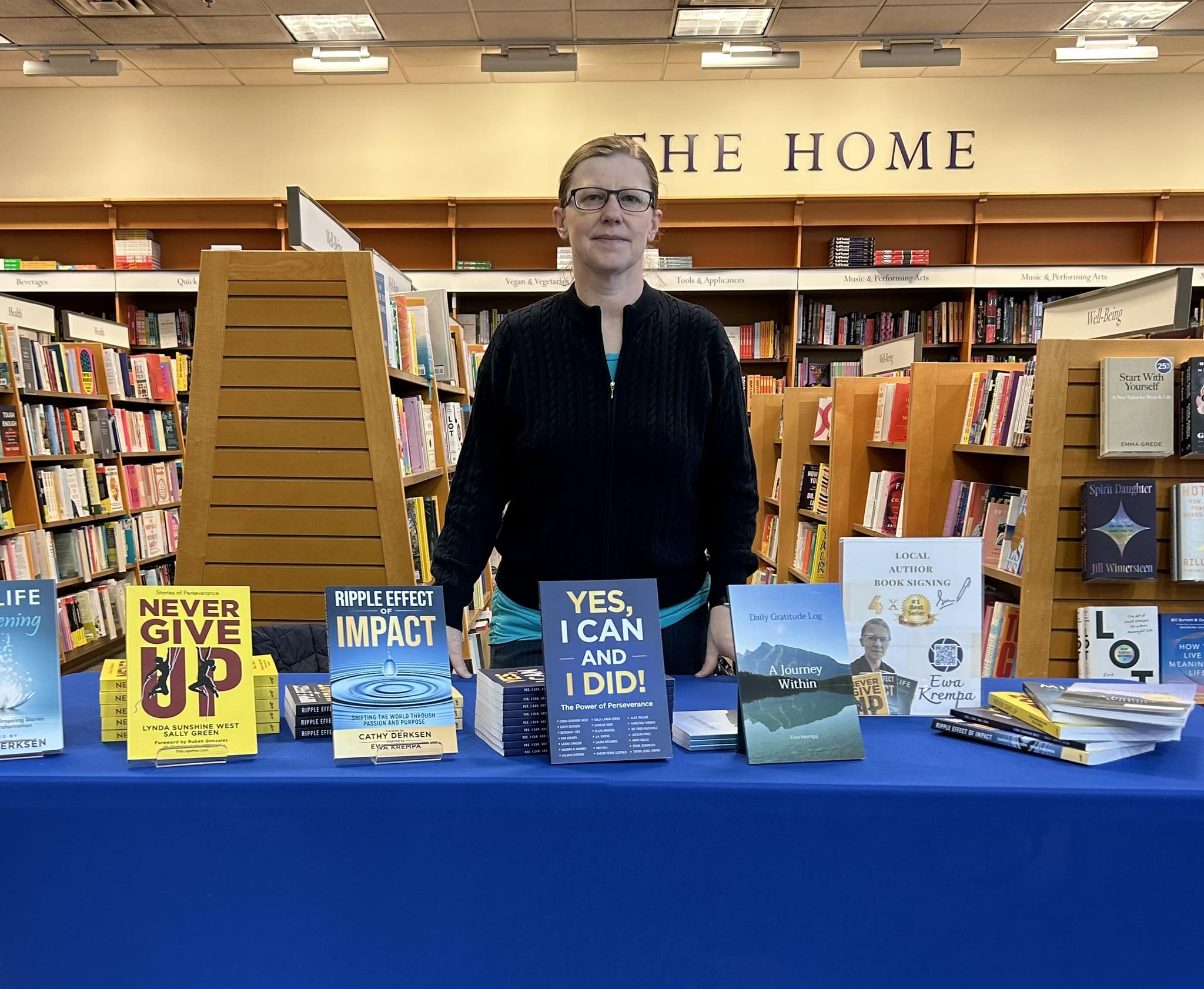 Person standing behind a table with books in a library, shelves in the background, and a sign reading 'THE HOME'.