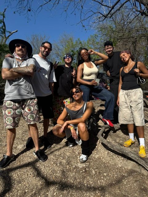 Group of seven people outdoors on a sunny day, standing and sitting on a rock, smiling and posing for the photo.