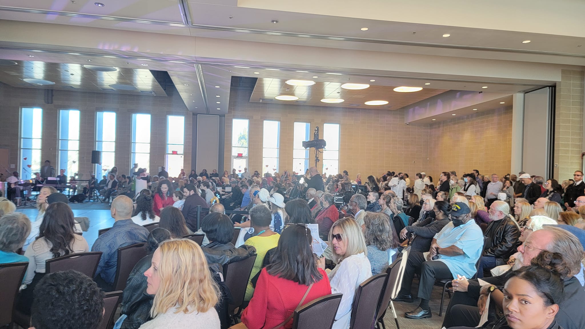 Large conference room filled with seated attendees facing a stage or presentation area, with tall windows in the background.