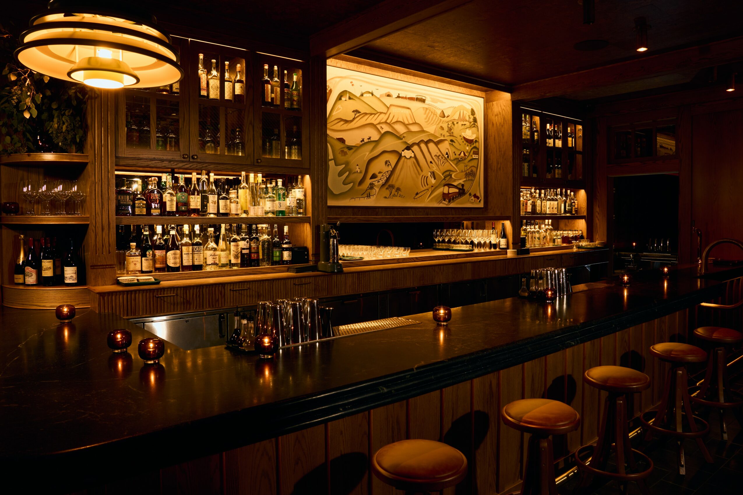 Bar interior with shelves of bottles, warm lighting, and a large framed artwork behind the counter.