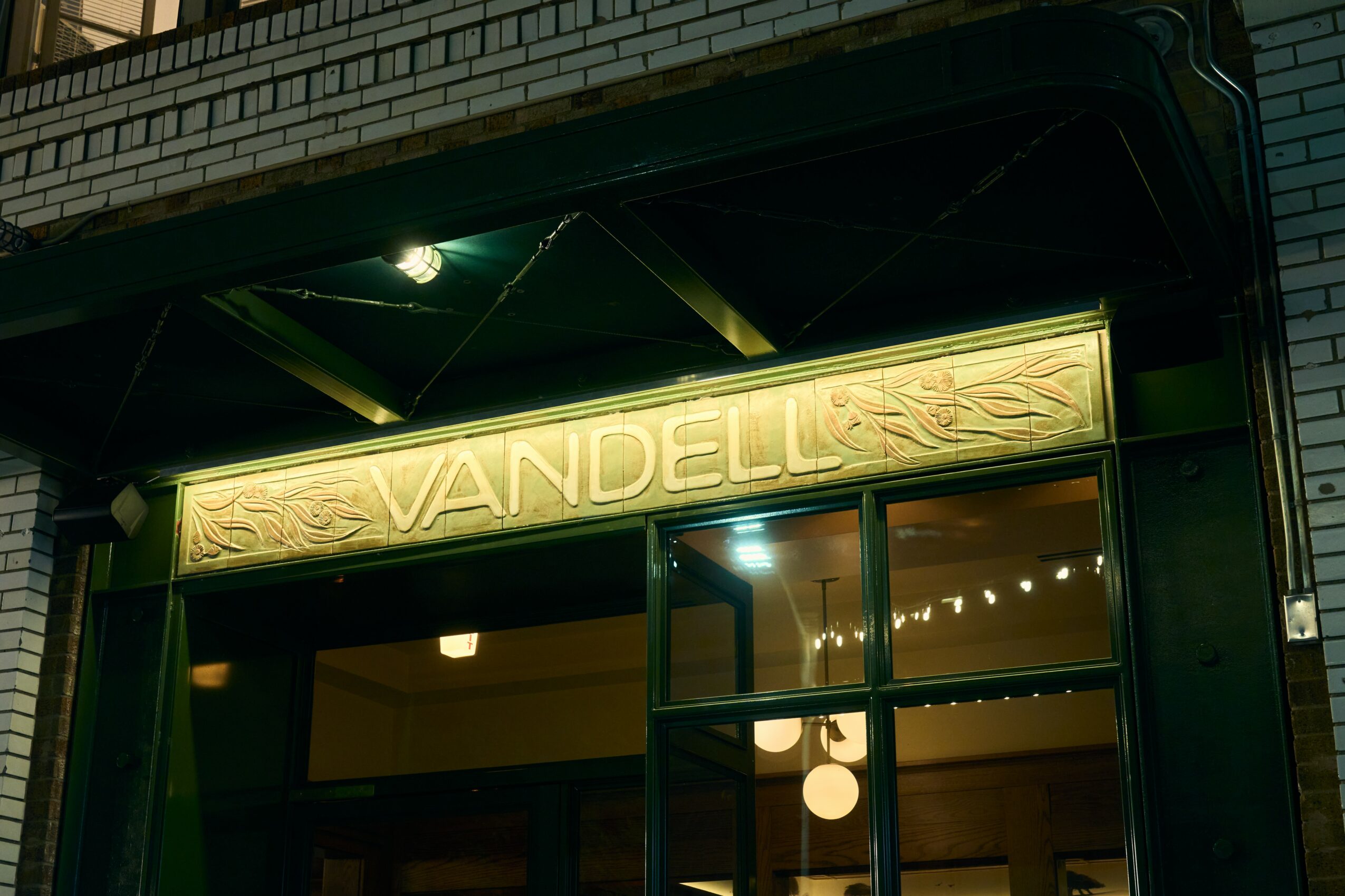 Storefront with illuminated sign reading 'VANDELL' above entrance, glass door, and brick exterior.