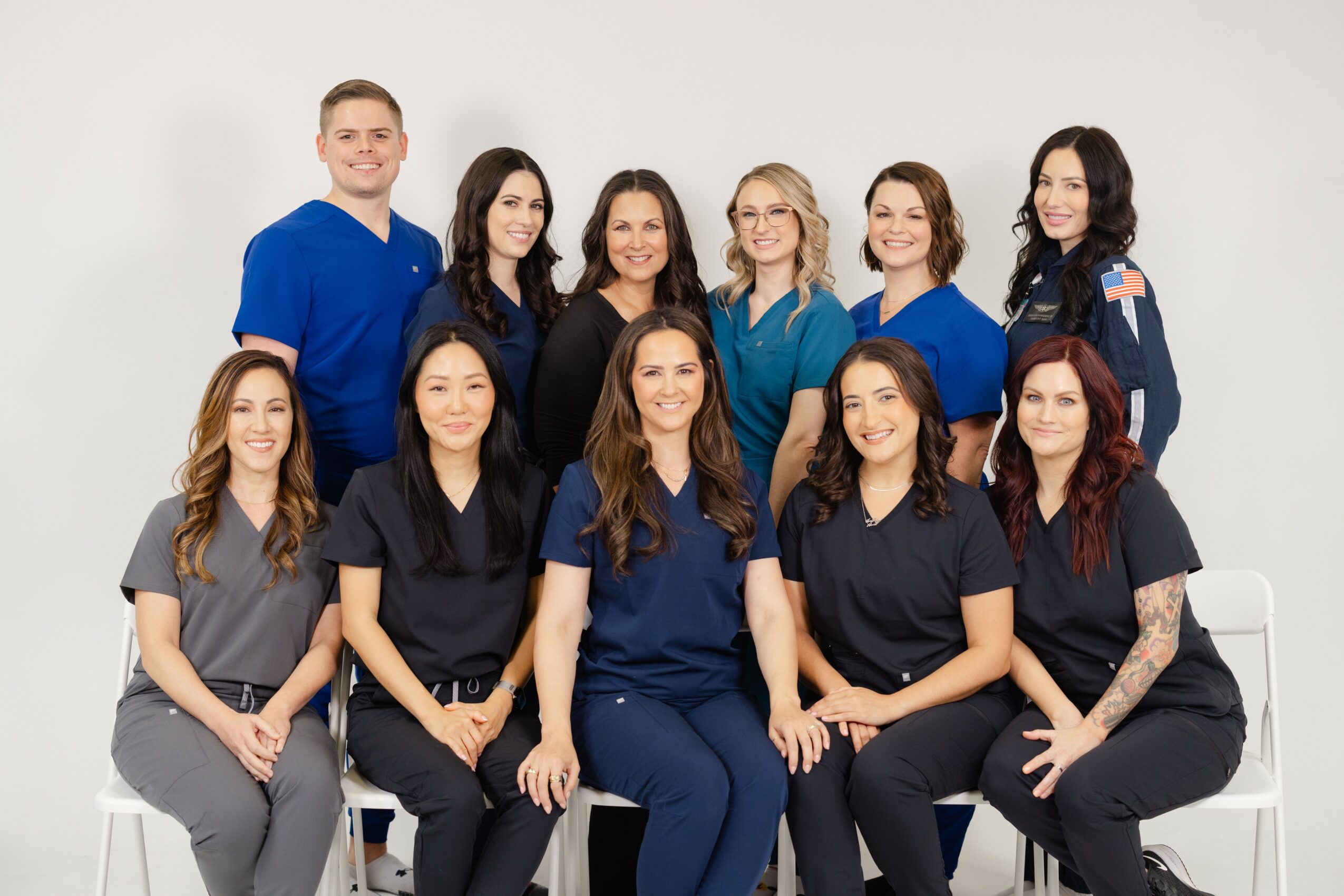 Group of ten women and one man posing together, some sitting and some standing, against a plain white background.