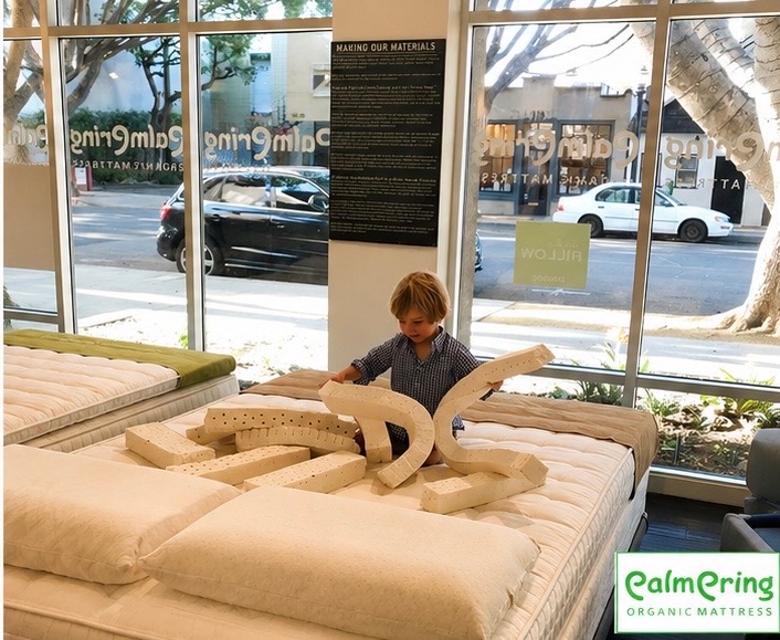 Child playing with large wooden blocks on a mattress inside a store, with large windows showing parked cars outside.