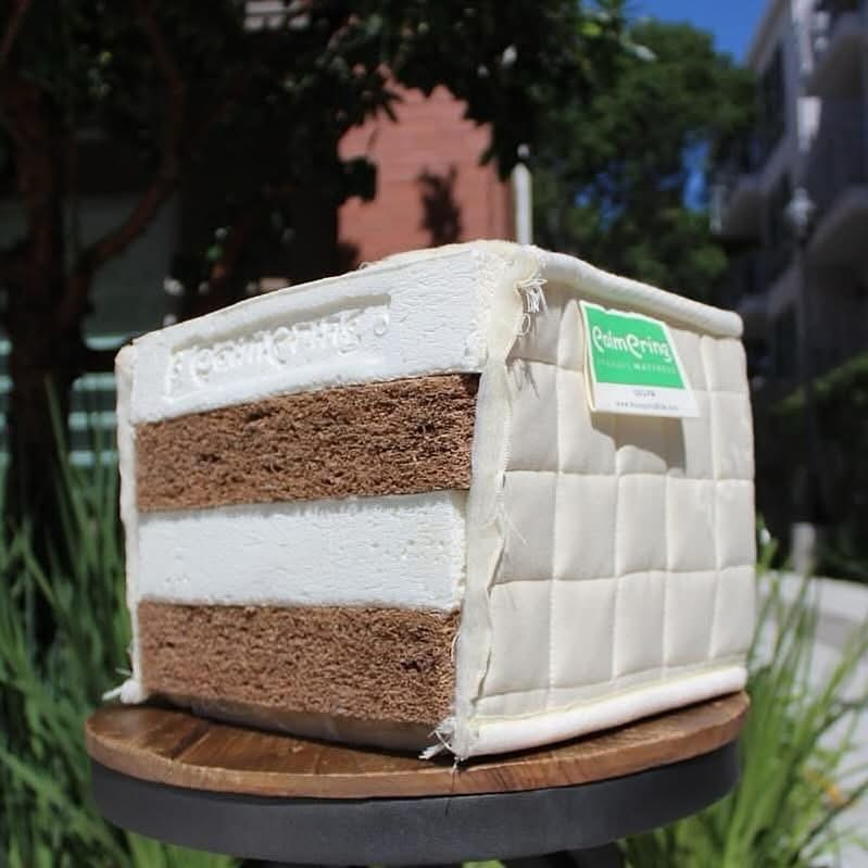 A cake with white and brown layers, decorated to resemble a small house, on a round wooden base outdoors.