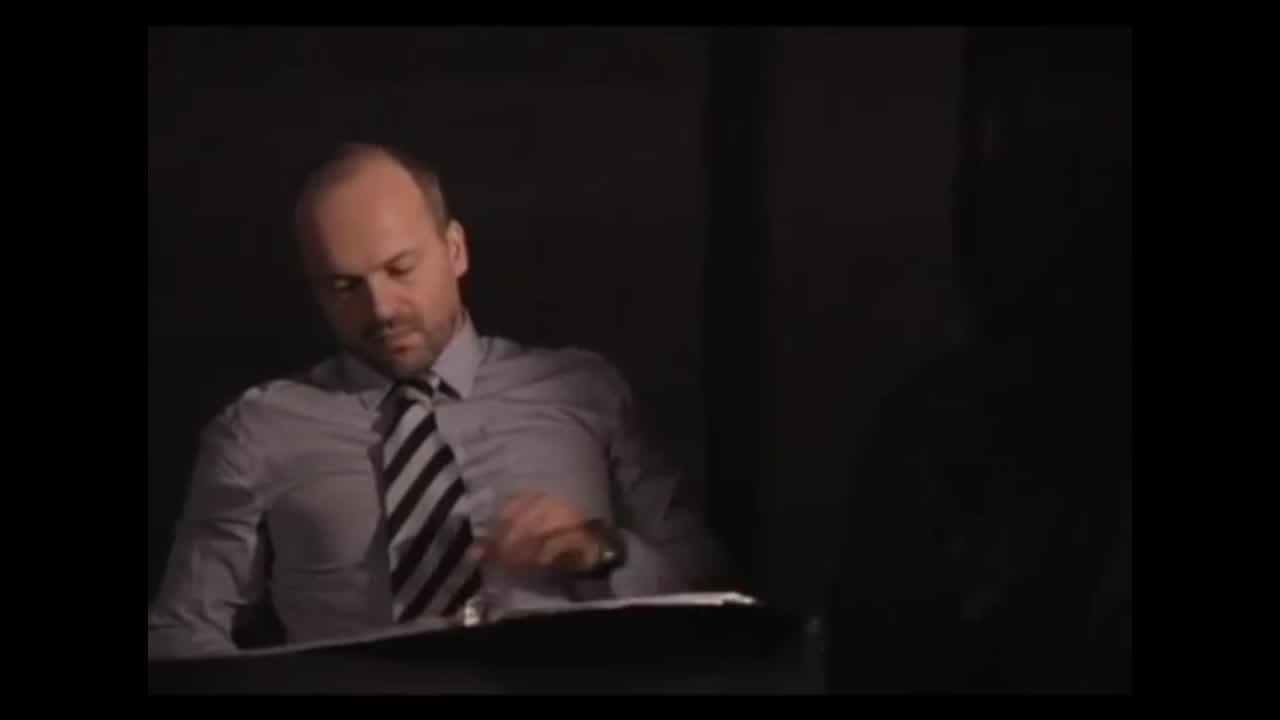 Man in a striped tie looking down at a tablet, dark background, focused expression.
