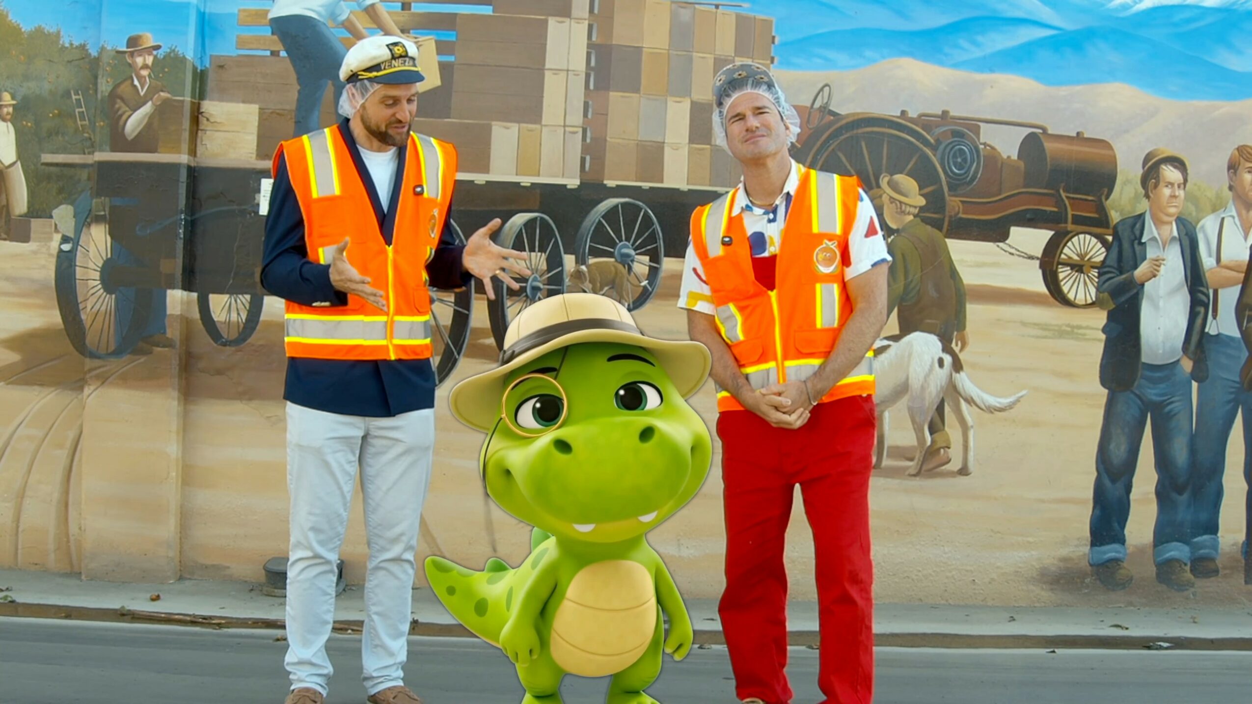 Two people in safety vests and a cartoon dinosaur character in front of a painted desert background.
