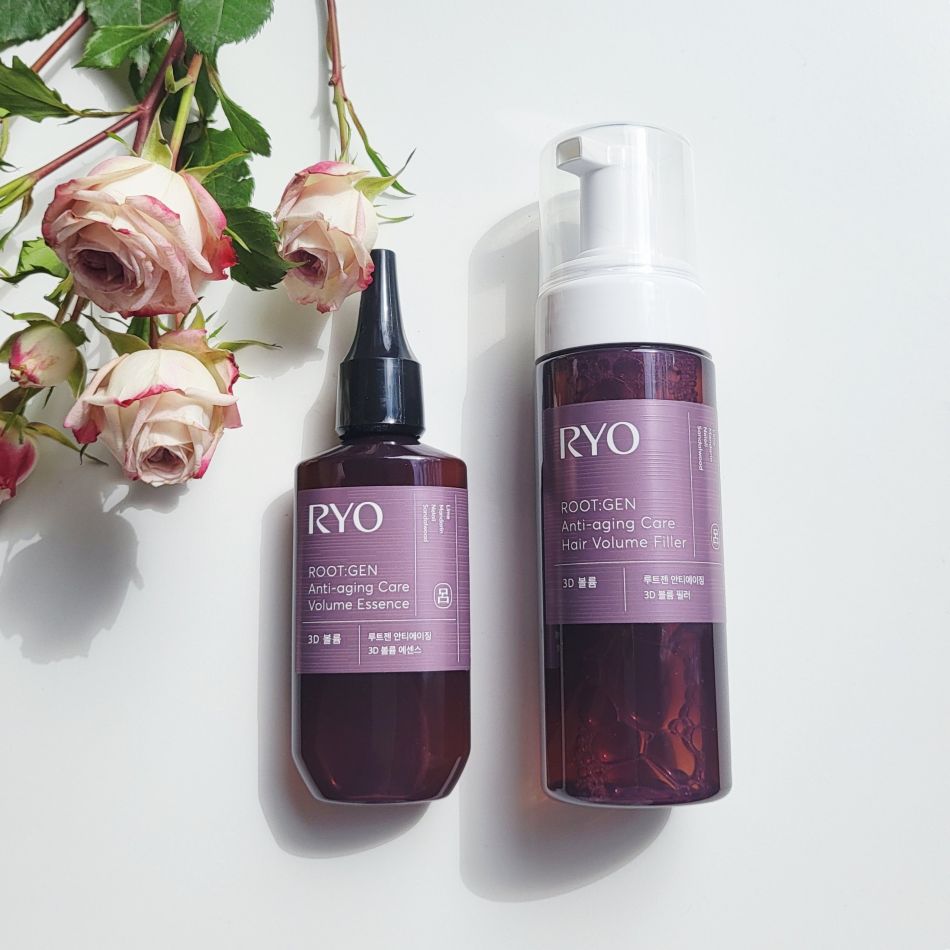 Two purple bottles of RYO root gel with a bouquet of pink roses beside them on a white surface.
