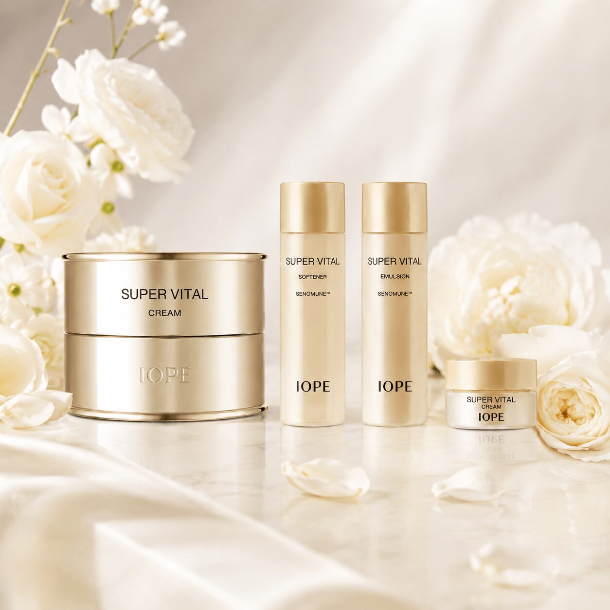Skincare products with white and gold packaging on a marble surface, surrounded by white flowers and petals.