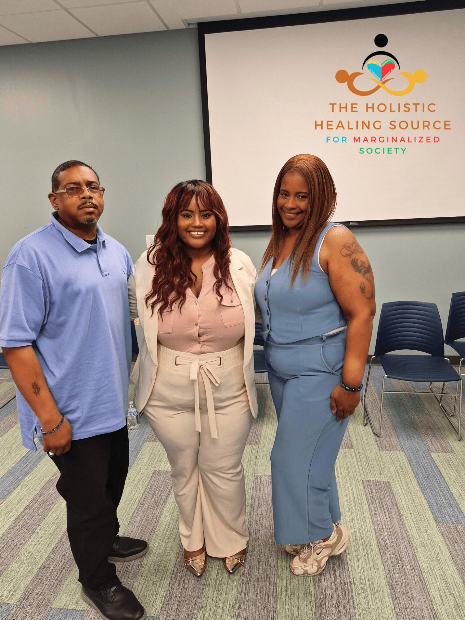 Three people standing in a room with a sign that reads 'The Holistic Healing Source' behind them.
