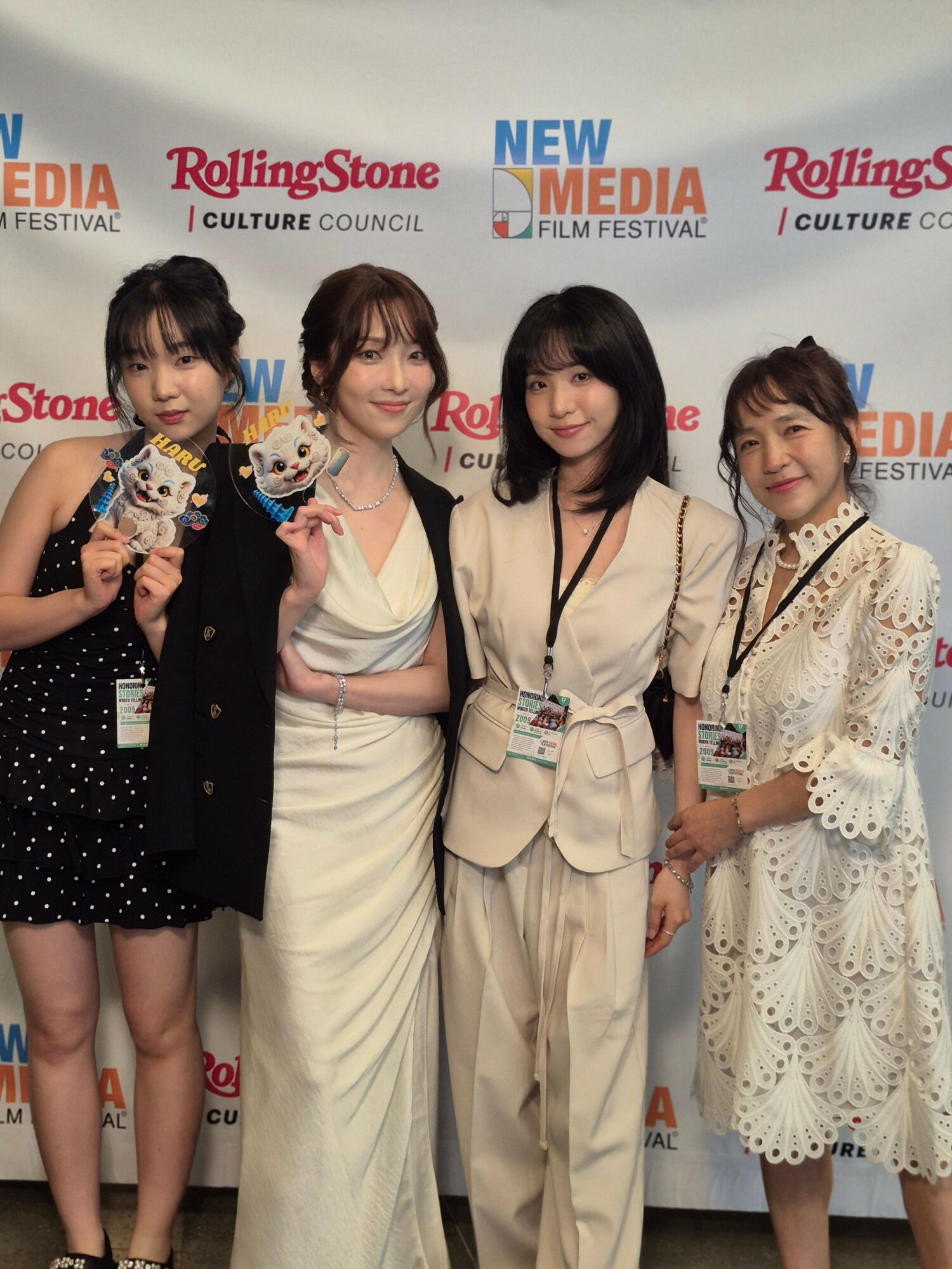 Four women standing together at an event, holding trophies, with a backdrop displaying logos and text.