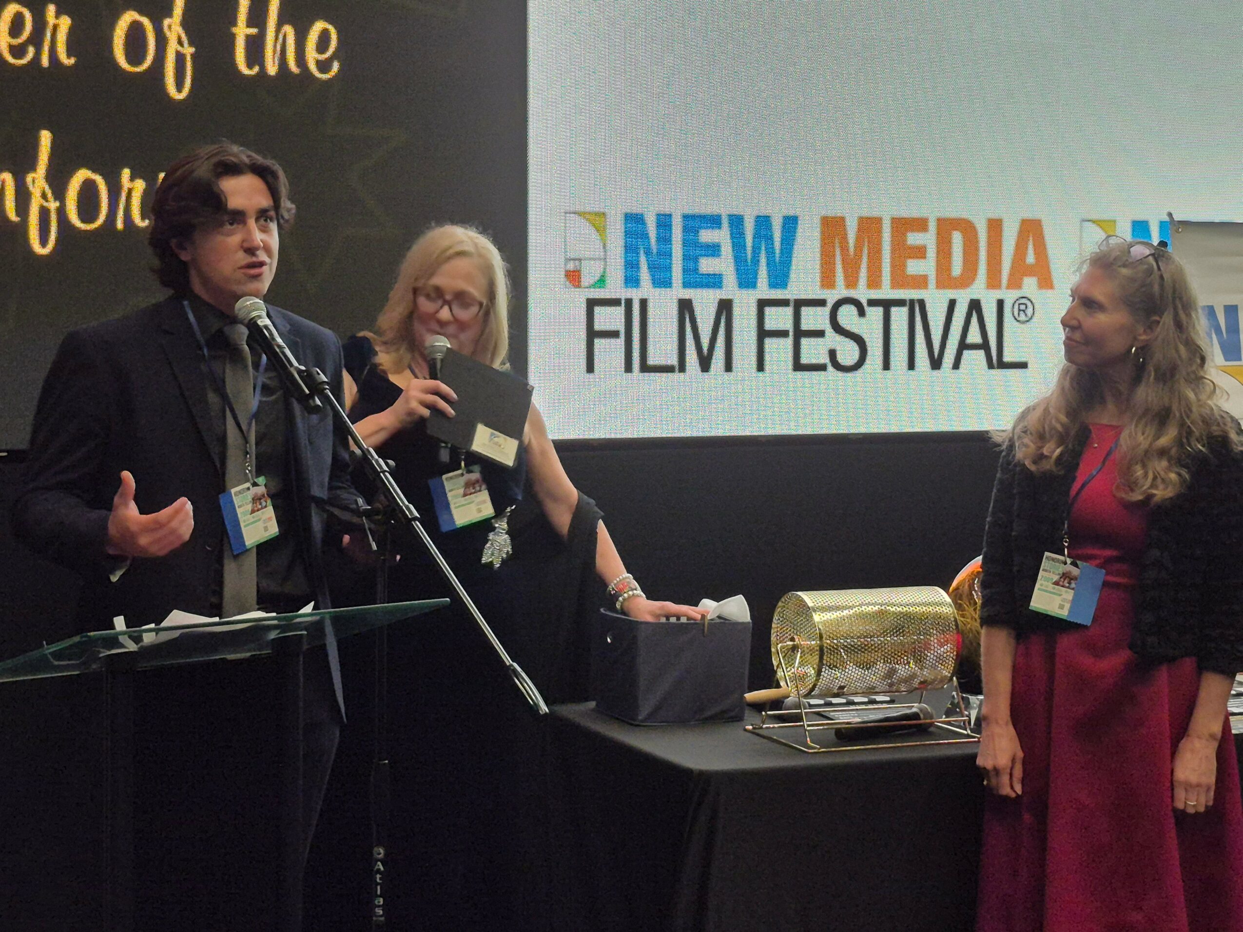 Three people on stage at a film festival, with a large screen displaying 'New Media Film Festival' behind them.