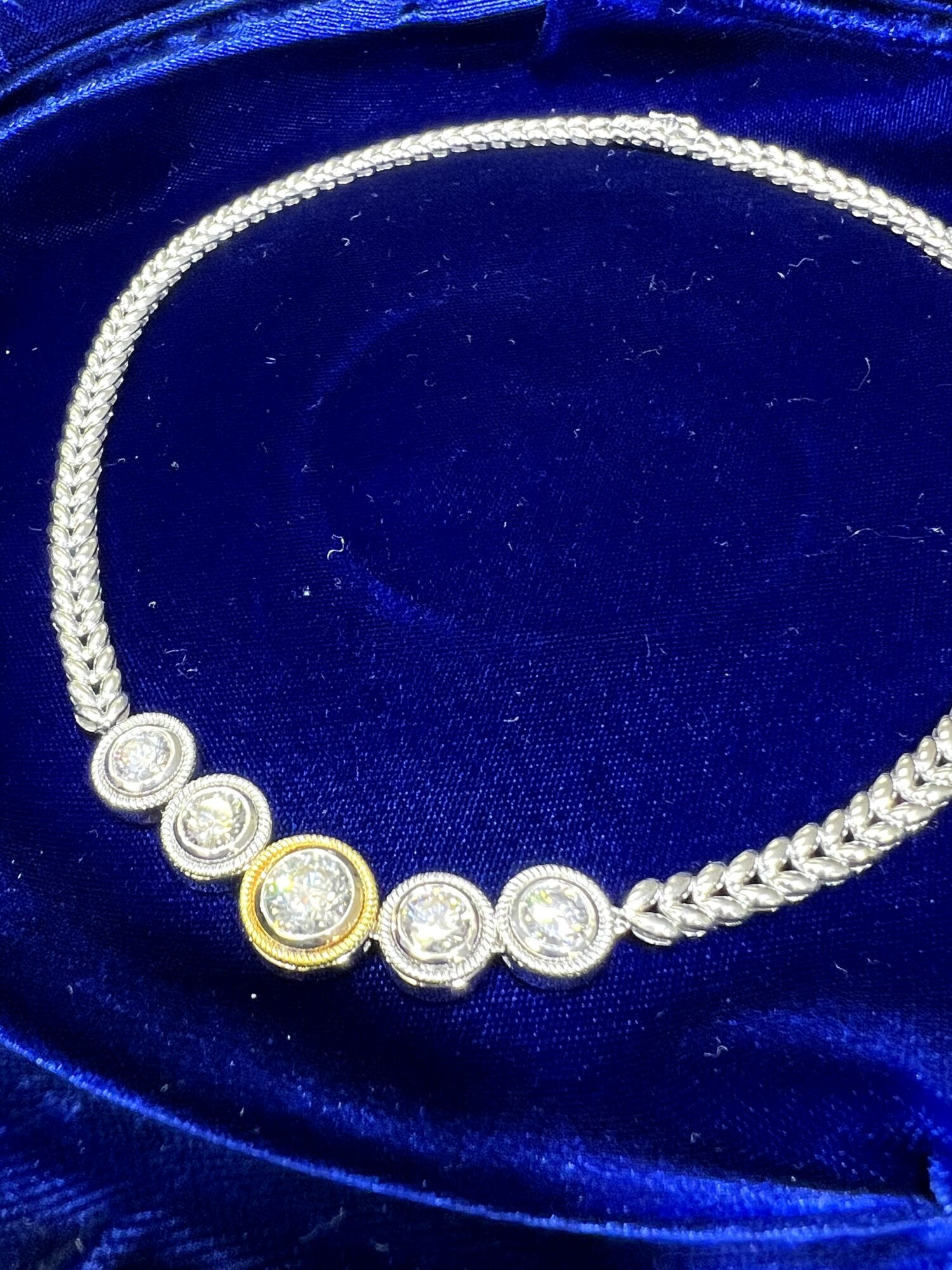 A diamond necklace with a series of round diamonds, some with gold accents, displayed on blue fabric.