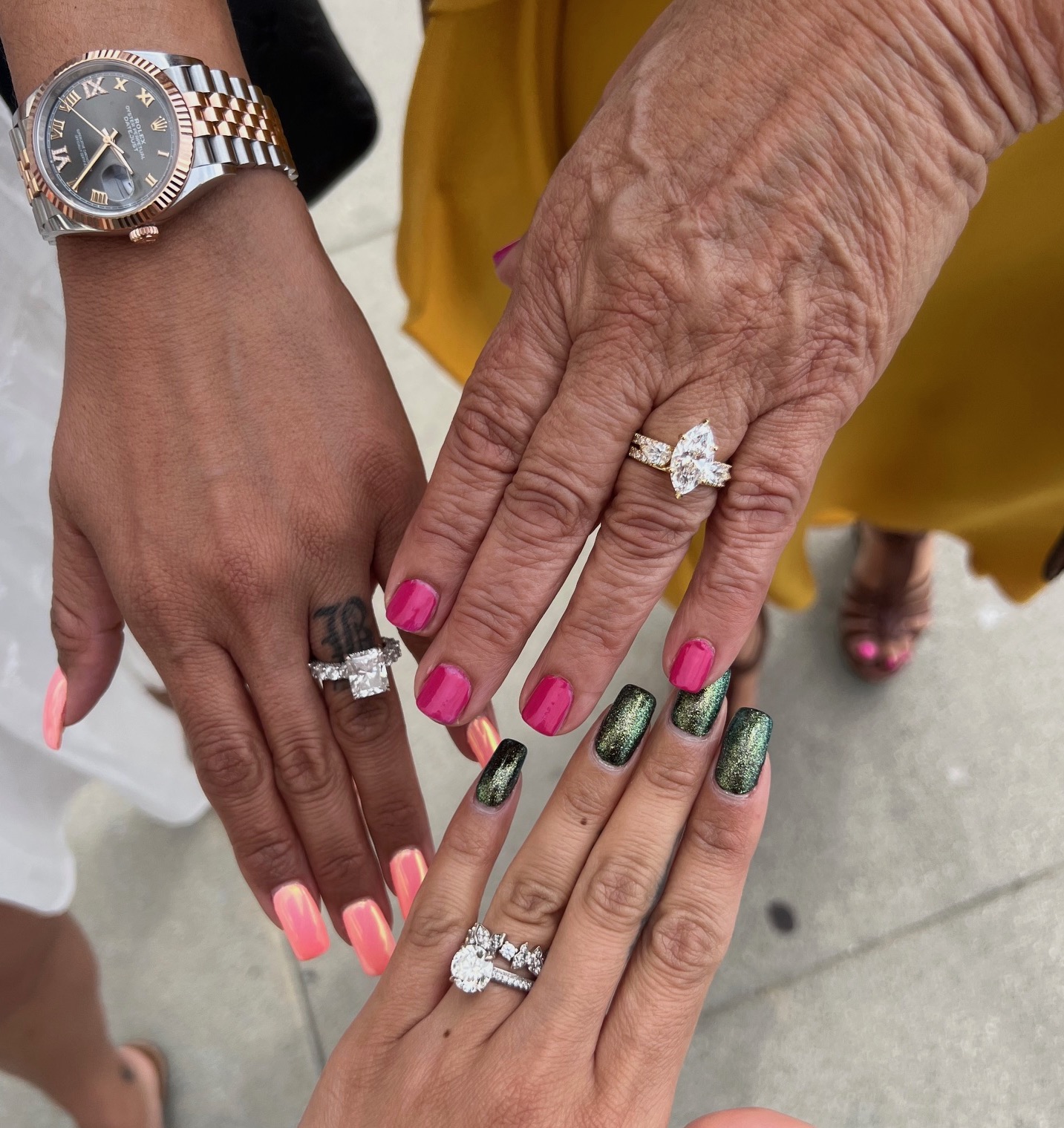 Three hands with rings and painted nails, one with a watch, on a gray surface.