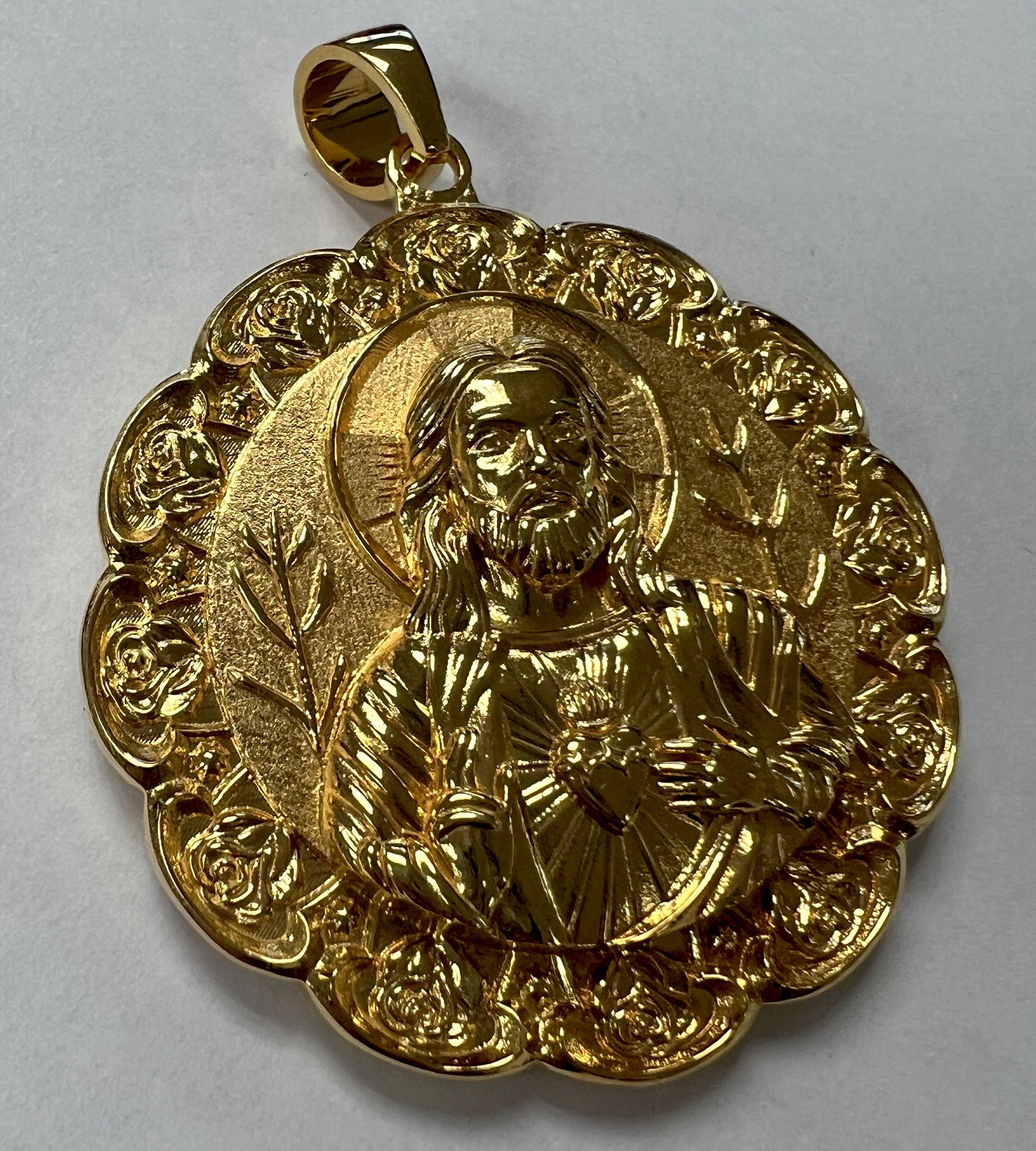 Gold religious pendant with a central figure of Jesus Christ surrounded by decorative floral patterns, on a plain background.